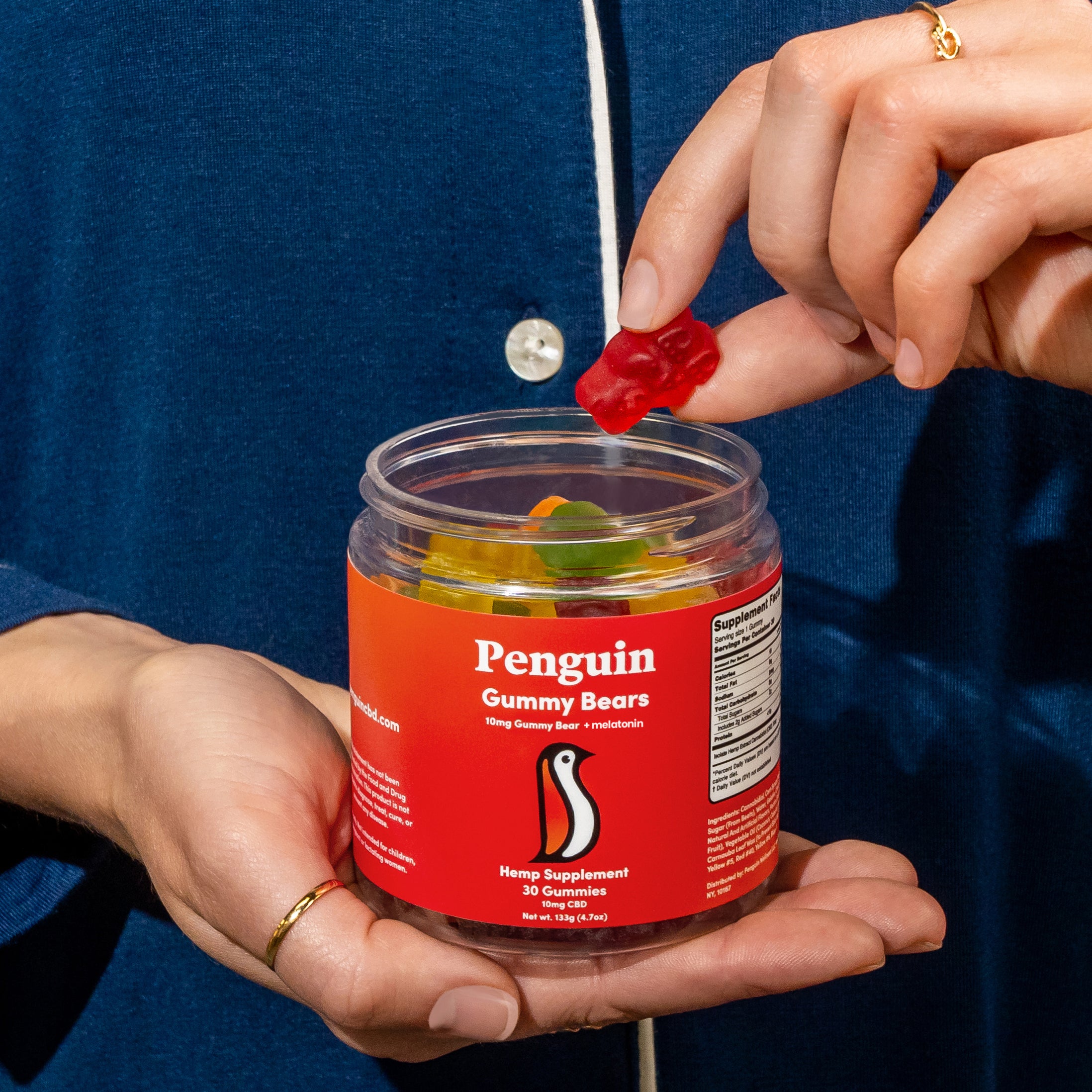 Person holding a jar of 'Penguin CBD Gummy Bears' with one being held above the jar.