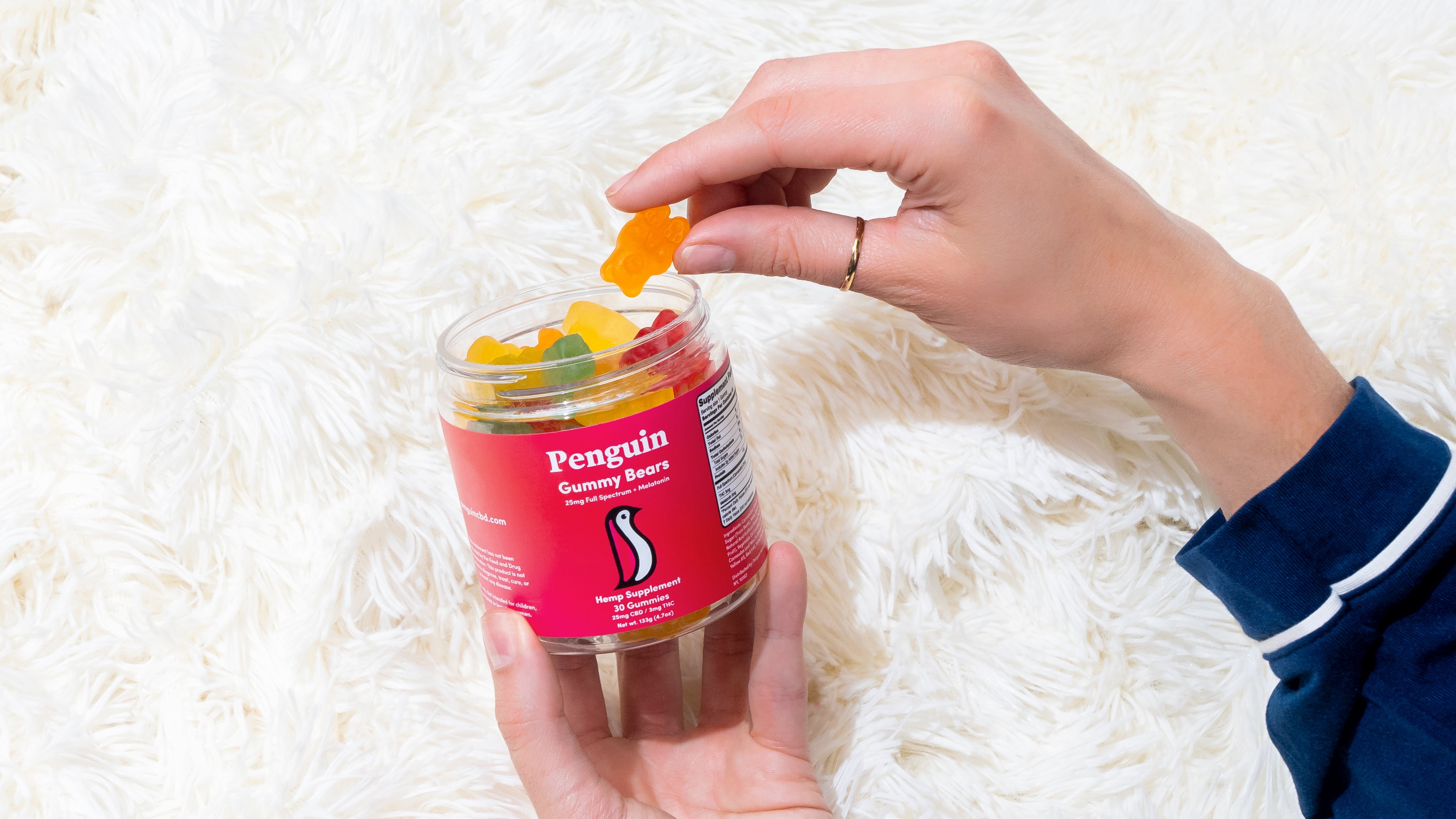 Person holding a jar of 'Penguin' gummy bears on a white fluffy surface