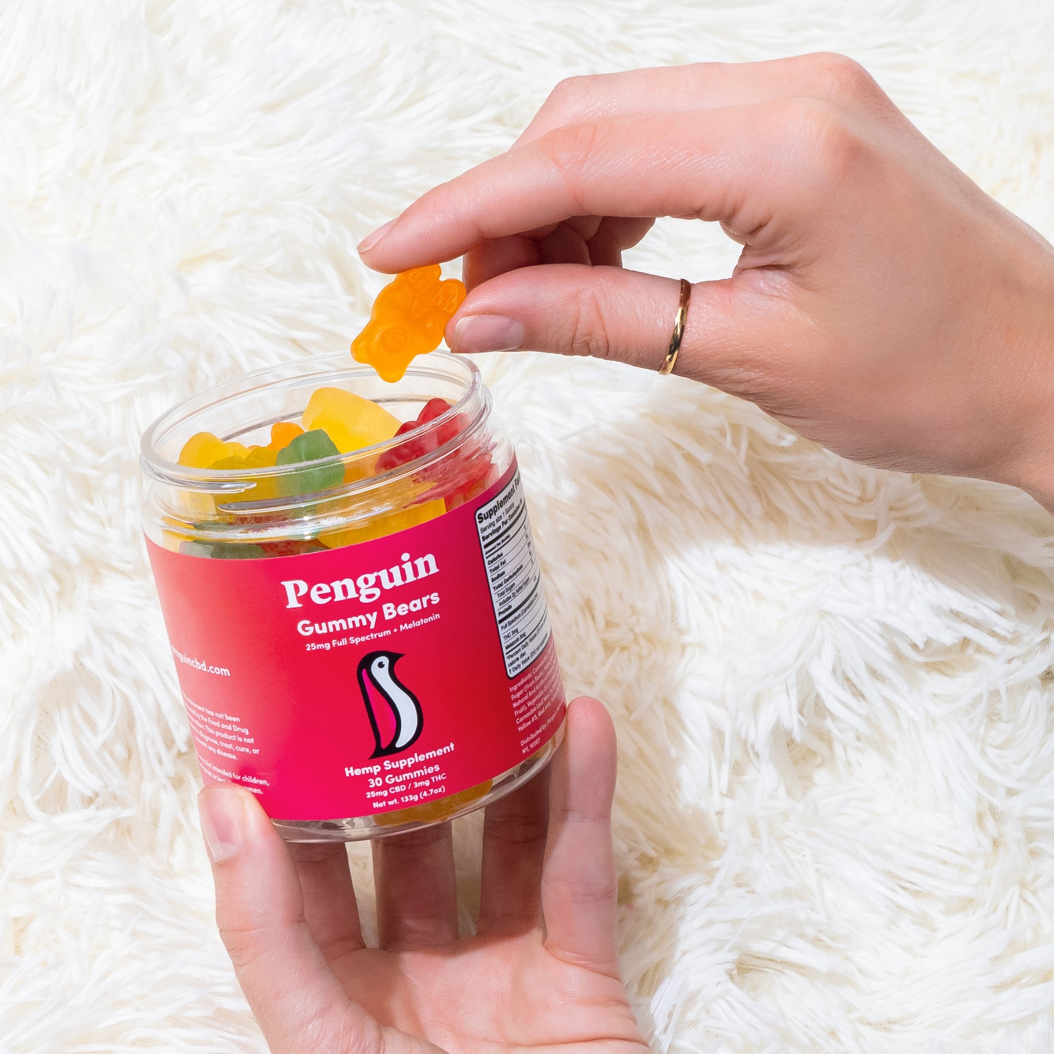 Hand holding a jar of Penguin Gummy Bears on a white fluffy surface