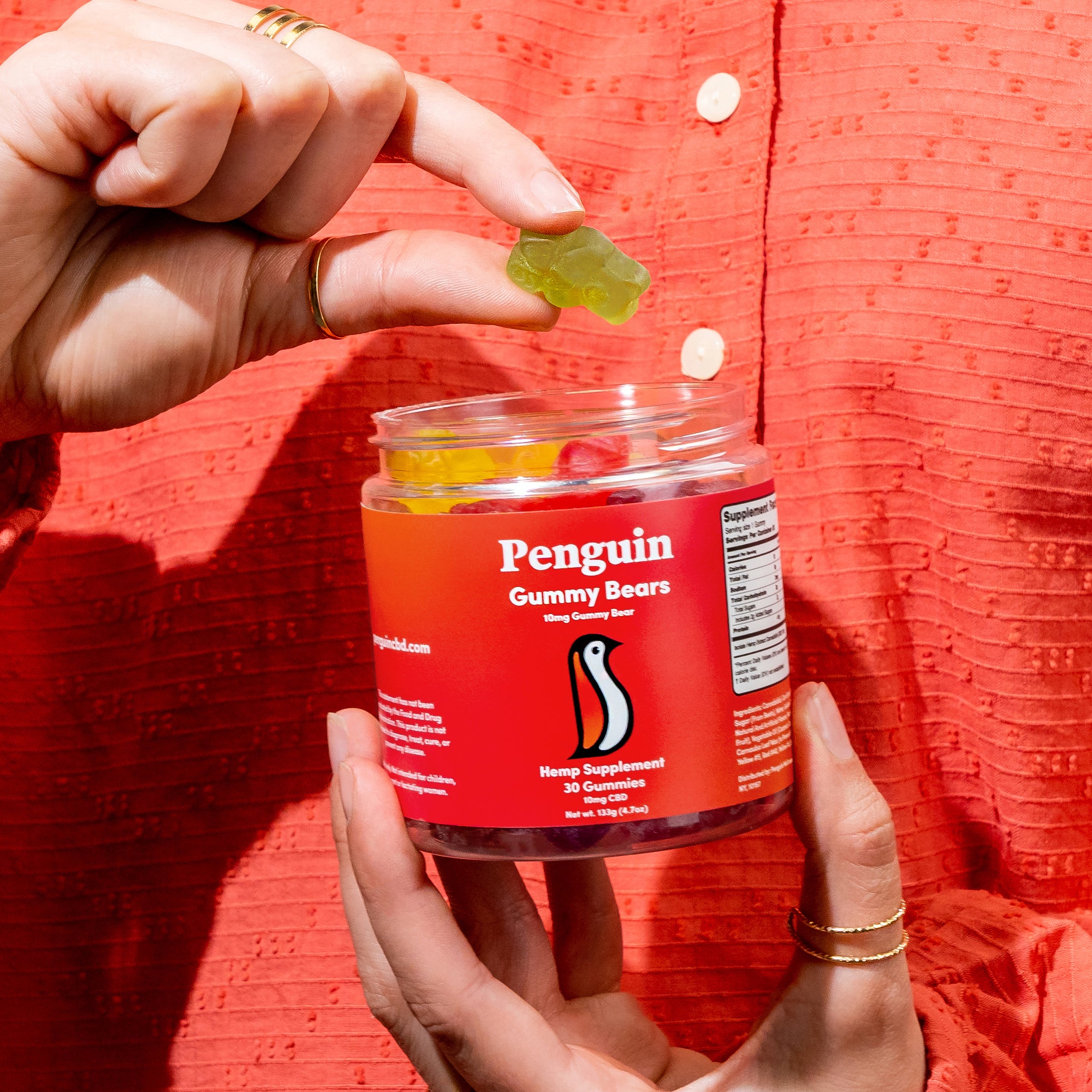 Person holding a jar of Penguin Gummy Bears against a red background